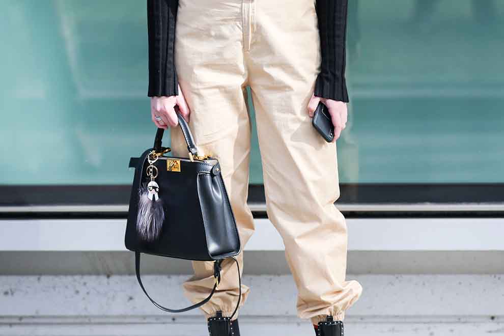 Pessoa com calças claras e bolsa preta elegante.