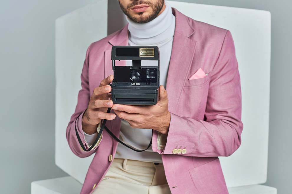 Homem vestindo terno rosa segurando câmera vintage
